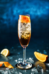 Fresh cocktail with champagne, orange and ice in wineglass on dark blue background. Summer cold drink and cocktail