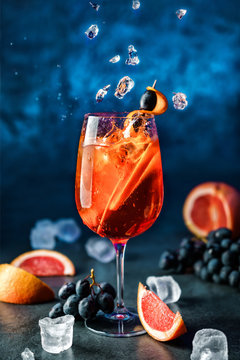 Naklejki Świeży grapefruitowy koktajl z pomarańcze, winogronami i lodem w wineglass na zmroku - błękitny tło. Strzał studio napoju w zamrożonym ruchu, latający lód, krople w plusk cieczy. Letni zimny napój i koktajl