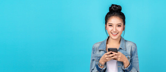 Banner of Portrait happy asian woman feeling happiness and looking camera holding smartphone on blue background. Cute asia girl smiling wearing casual jeans shirt and connect internet shopping online