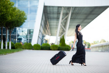 Smiling female passenger proceeding pulling suitcase through airport
