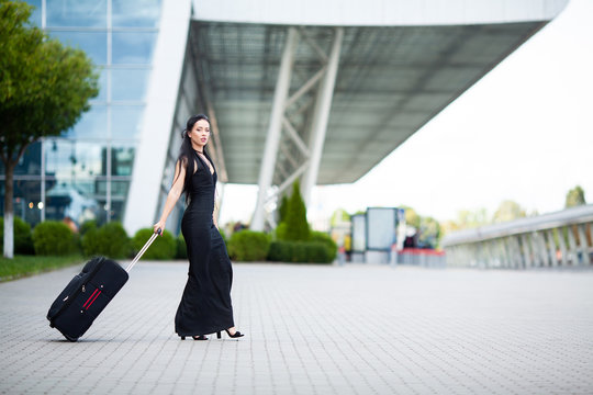 Smiling female passenger proceeding pulling suitcase through airport