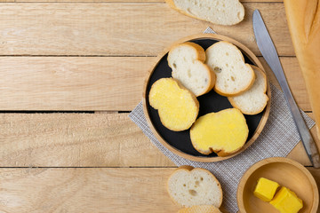 Sliced baguettes on wooden dish with butter on the wooden table.
