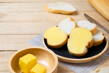 Sliced baguettes on wooden dish with butter on the wooden table.