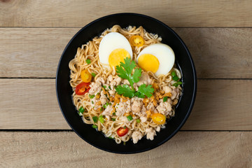 Bowl of instant noodle with minced chicken and boiled egg on wooden table.