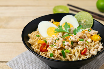 Bowl of instant noodle with minced chicken and boiled egg on wooden table.