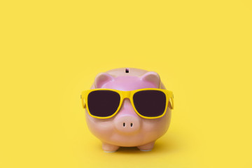A pink piggy bank in sun glasses at a party. Yellow background.