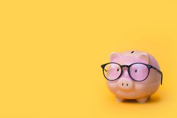 A pink piggy bank in glasses. Yellow background.