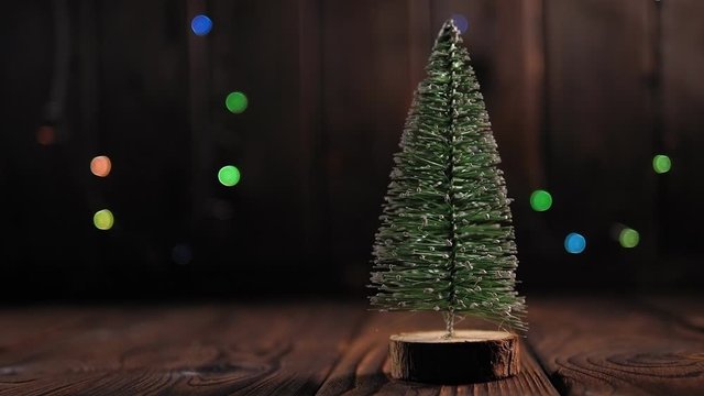 A small Christmas tree on a wooden background with colorful flashing lights. Slow motion. Copy space. Christmas background.