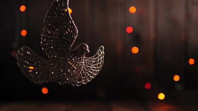 Golden Christmas dove on a wooden background with flashing lights. Christmas decorations on a wooden background. Christmas toy on a branch. Dove of peace.