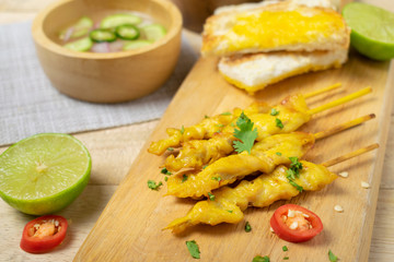 Grilled chicken satay on skewers with toast and bowl of sauce on the wooden table.