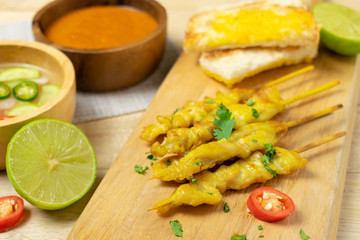 Grilled chicken satay on skewers with toast and bowl of sauce on the wooden table.