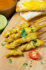 Grilled chicken satay on skewers with toast and bowl of sauce on the wooden table.