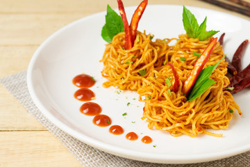 Instant noodles with dry chili and tomato sauce in white dish on wooden table.