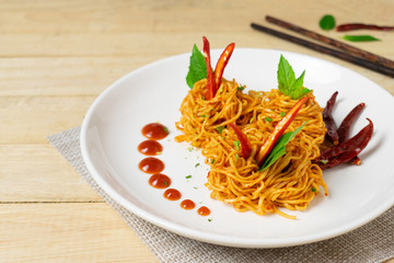 Instant noodles with dry chili and tomato sauce in white dish on wooden table.