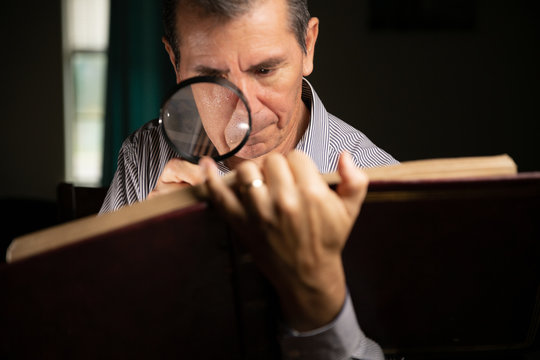 Mature man with glasses at home watching an old photo album remembering the past and looking at the pictures with a magnifying glass