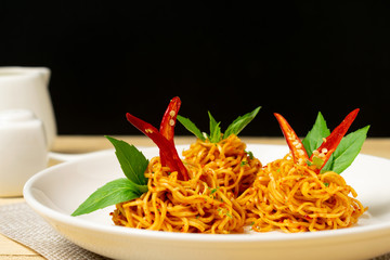 Instant noodles with dry chili and tomato sauce in white dish on wooden table.
