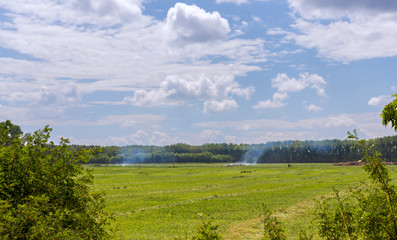Fototapeta na wymiar summer landscape, agriculture burn trash in the fields smoke comes from bonfires against a bright blue sky with clouds on a sunny day
