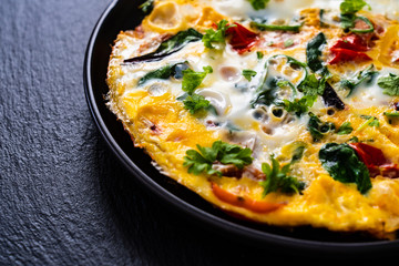 Breakfast - scrambled eggs with vegetables on black stone background