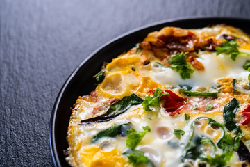 Breakfast - scrambled eggs with vegetables on black stone background