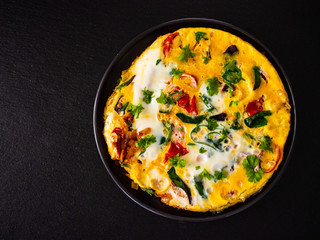 Breakfast - scrambled eggs with vegetables on black stone background