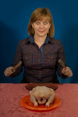 Woman tries to eat a crude chicken. Sits at a table with a knife and a fork, plug. On a plate a...