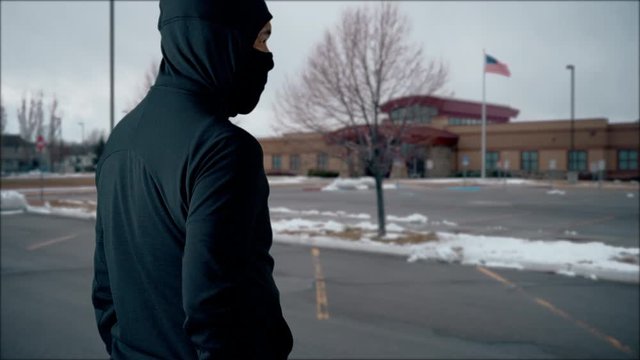 Killer, thief or terrorist wearing a mask outside a school, hospital or some other public building branishing a large knife in a threatening way - winter, static, wide angle