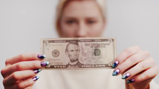 Extreme close up shot of female hands holding five dollar bill. Slow motion shot with a blond woman, blurred background with copy space