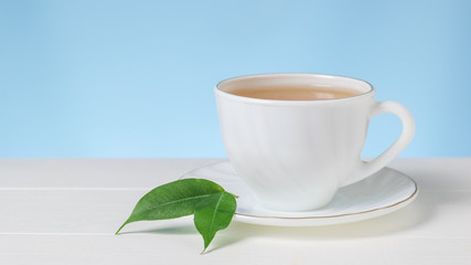 Two green leaves on a white Cup of tea on a white table.