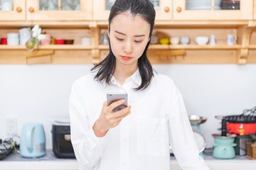 キッチンで携帯電話を操作する女性