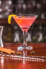 Cosmopolinan coctail on a wooden stand. Bar accessories: shaker, spoon, spices on a wooden stand