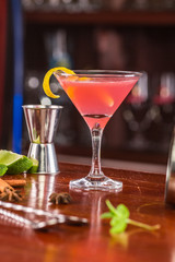 Cosmo coctail on a wooden stand. Bar accessories: shaker, spoon, spices on a wooden stand