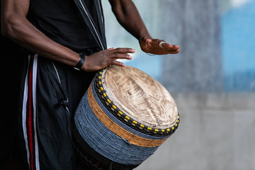 Closeup of african male artist wearing stripped pant and playing traditional african djembe drums...