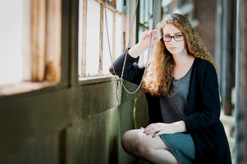 young woman with curly hair and black glasses sitting in front of sunlit window