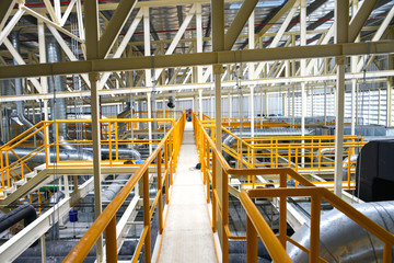Industrial walk way with yellow handrail and steel structure roof inside factory.