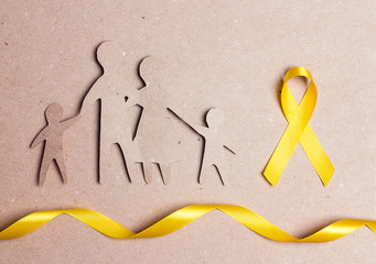 Cardboard silhouette of a family with yellow awareness ribbon on cardboard background.