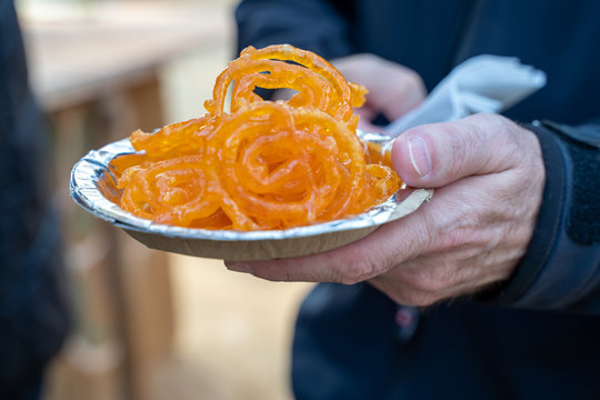 Caucasian male hand holds a plate of Jalebi (tradtional Indian fried sweet dessert) at a festival, in selective focus