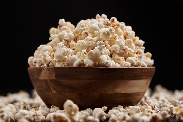 Wooden bowl with salty popcorn on a wooden table. Dark background Selective focus.