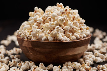 Wooden bowl with salty popcorn on a wooden table. Dark background Selective focus.