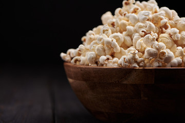 Wooden bowl with salty popcorn on a wooden table. Dark background Selective focus.
