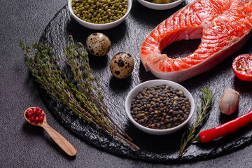Raw trout red fish steak served with herbs and lemon and olive oil on a dark background