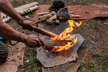 Man hand with wooden sticks igniting burning flame to keep fire alive on gray slate during...