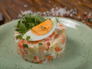 Olivier salad on a plate on a brown wooden table, studio light