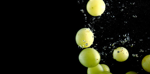 Green grape falling into water at black background