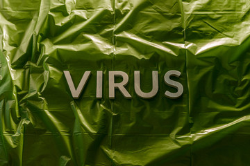 the word virus laid with silver metal letters on green crumpled plastic film with dramatic light