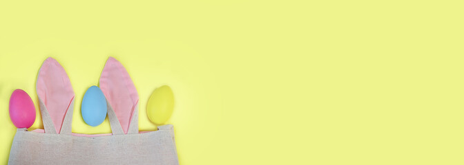 bag with Easter bunny ears and Easter eggs on a yellow background, banner. For postcards, design.copy space