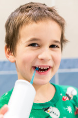 a 5-year-old boy at home washes his teeth with an oral irrigator. Little boy cleaning teeth with oral irrigator. Dental Care Concept. Oral Care Concept. vertical photo