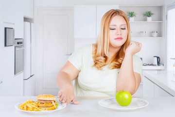 Overweight woman rejecting fast foods in kitchen