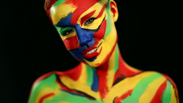 Woman with color face art and body paint. Colorful portrait of the girl with bright make-up and bodyart. Slowmotion.