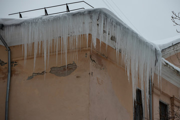 Icicle on the roof. Building covered with big icicles. Icicles hang from the roof, ice stalactite hanging from roof