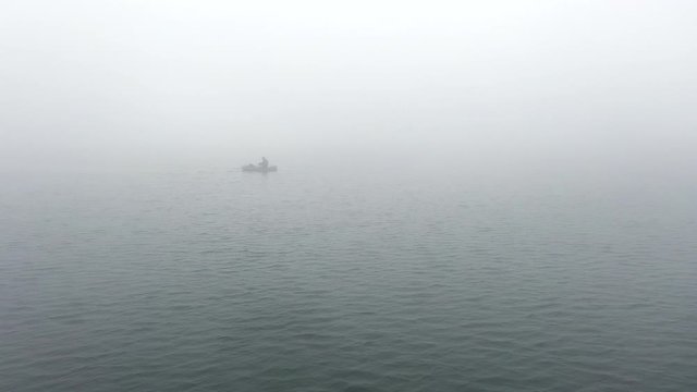 Fisherman in a rubber boat on lake in the fog